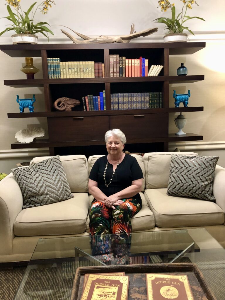 Dr. Janet P Littlejohn sitting on cream sofa in front of bookshelves.